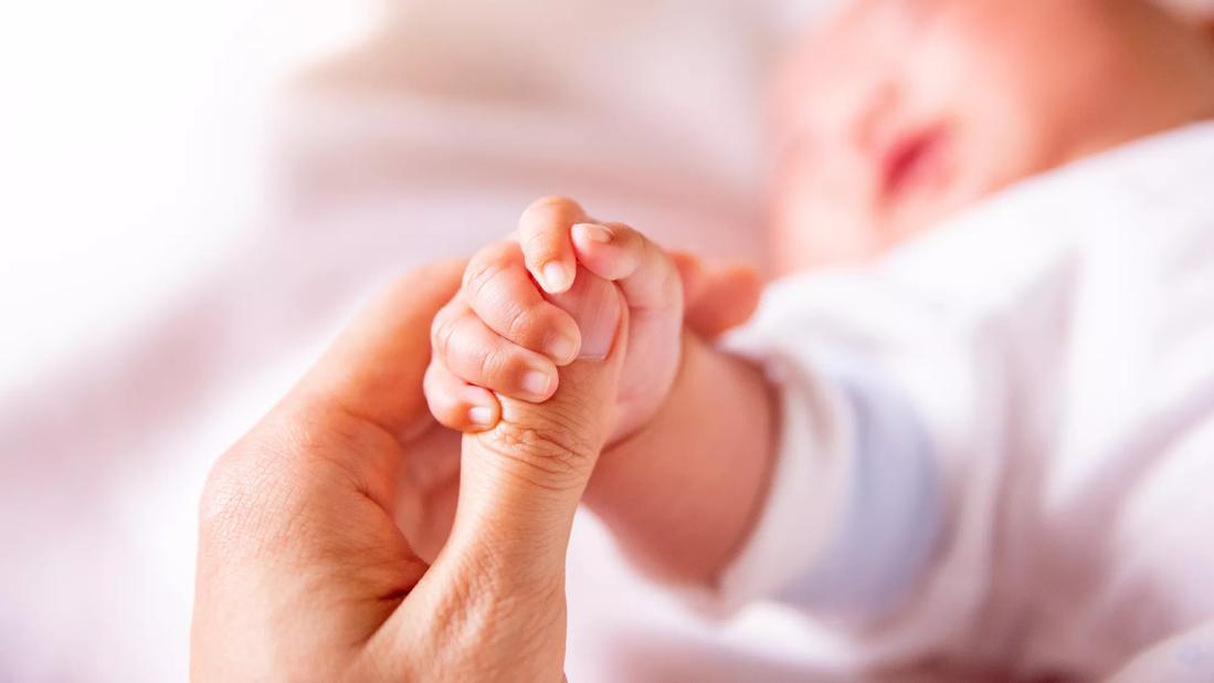 Newborn's tiny hand gripping caregiver's thumb