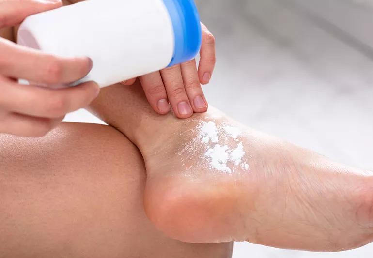 Applying foot powder to clean feet to cut down on odor.