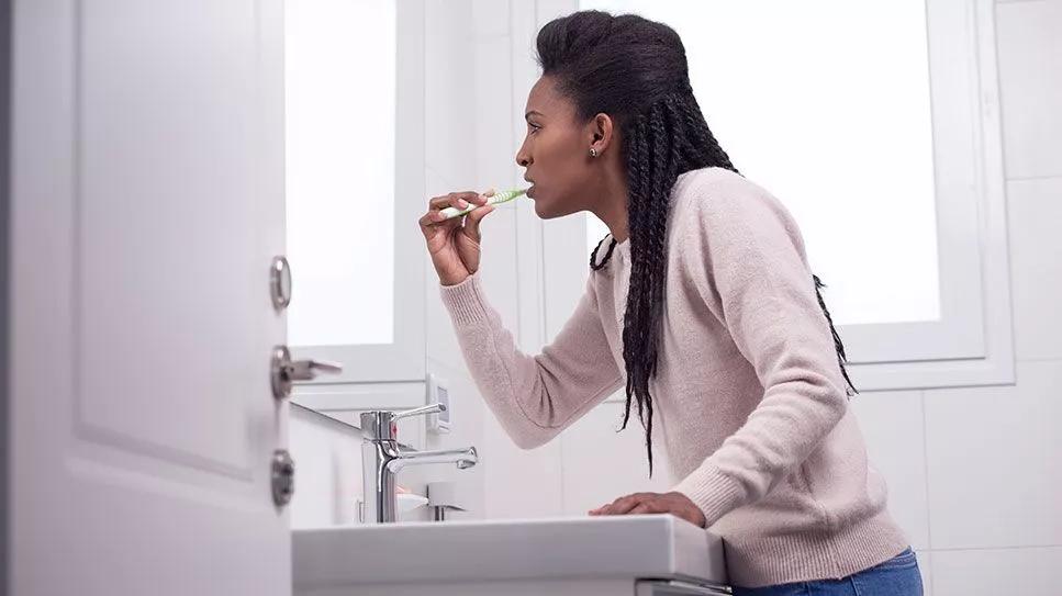 person leaning over sink brushing teeth