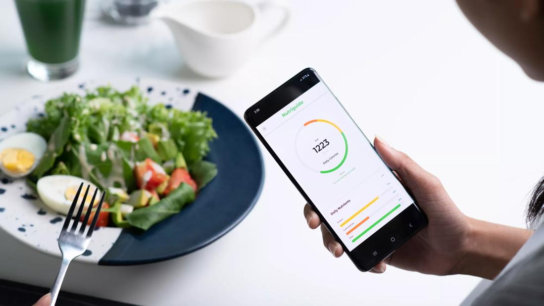 Person monitoring nutritional intake on smartphone app while eating a salad