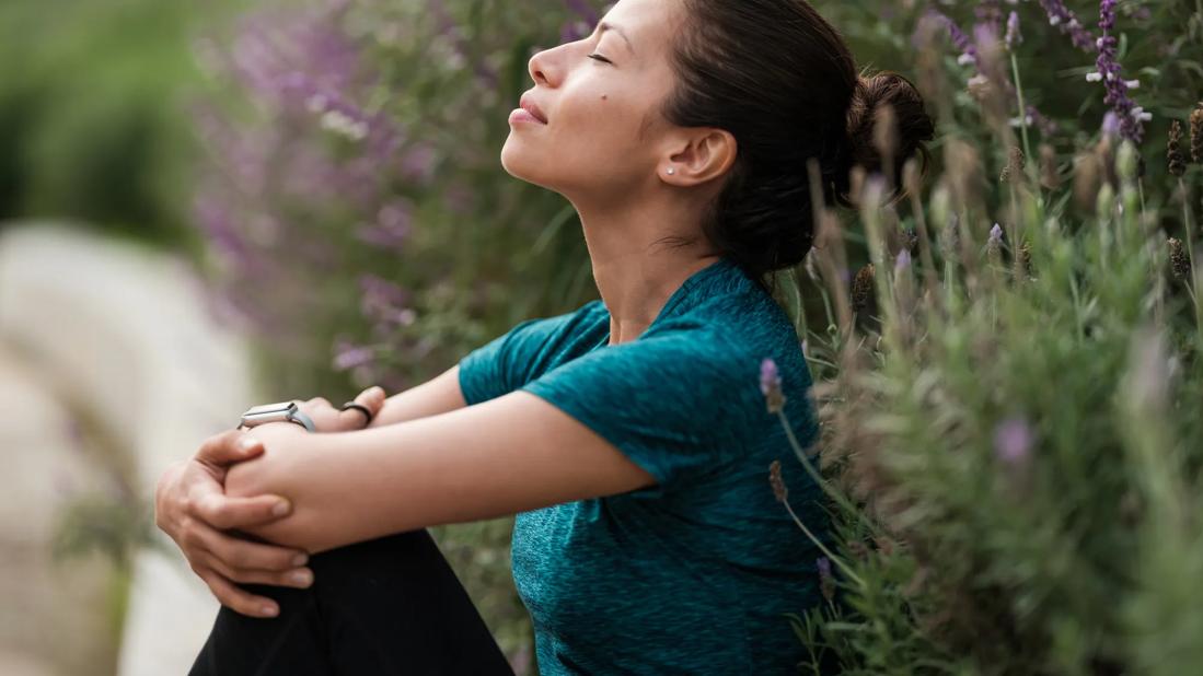 Person relaxing, head back, eyes closed, sitting in patch of purple flora