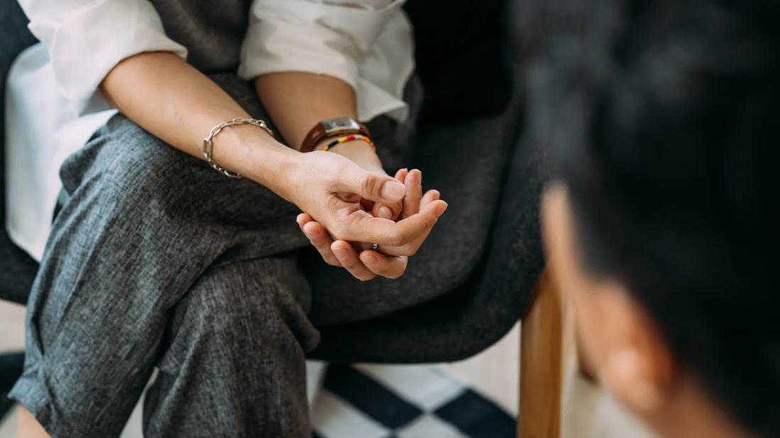 Close-up of hands of person sitting, legs crossed, facing another person