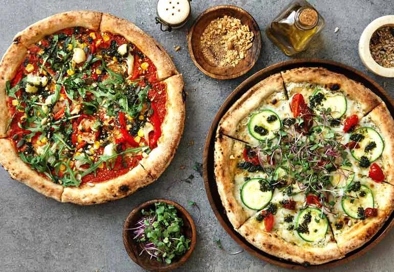 Two vegetarian pizza with a variety of healthy toppings on a granite table seen from above.