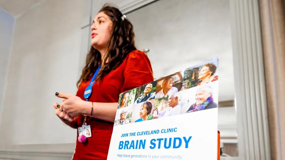 woman in red shirt standing beside a sign for clinical study recruitment