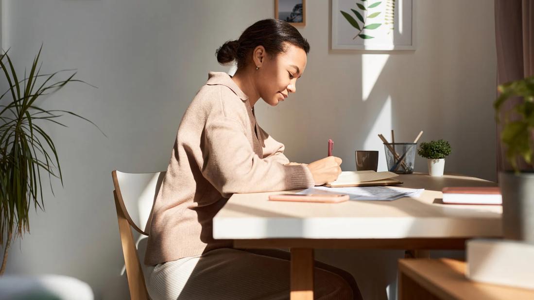 Person sitting at home desk writing in a journal