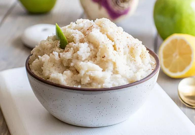 A bowl holds a mound of cooked mashed turnips and Granny Smith apples that have been blended together.