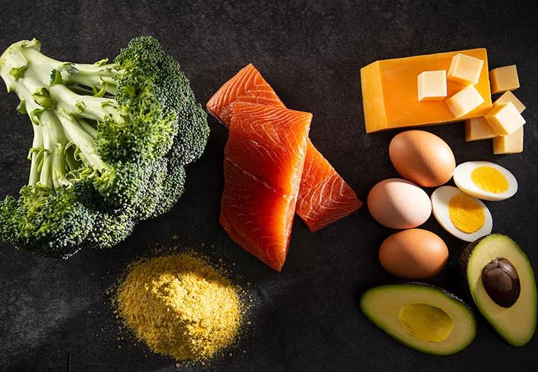 Table arrayed with broccoli, salmon, cheese, eggs, avocados, and nutritional yeast