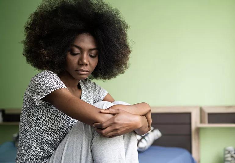 A person sits on the edge of their bed exhausted after working the night shift.