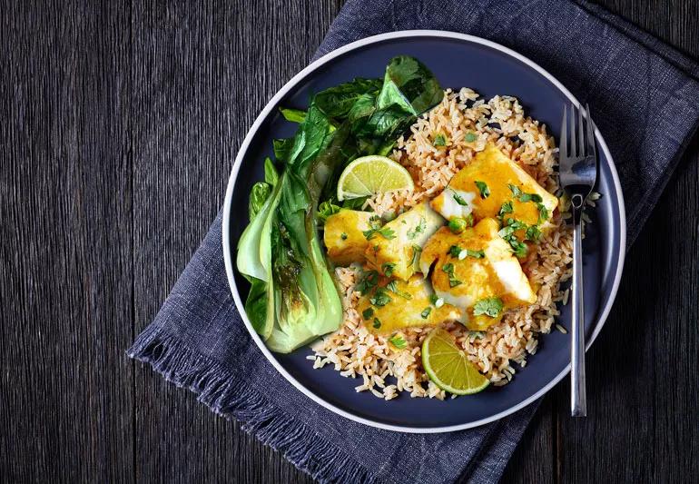 A plate of curried cod on a bed of brown rice with bok choy as the vegetable.