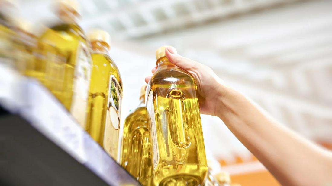 Person lifting bottle of olive oil off grocery store shelf