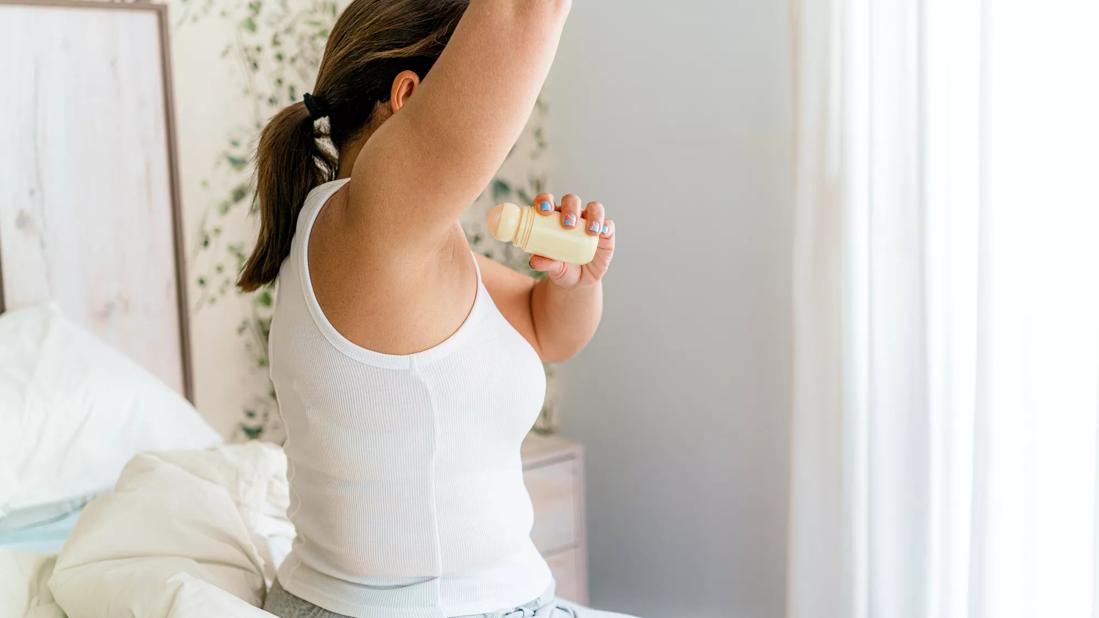 Person sitting on bed applying antiperspirant