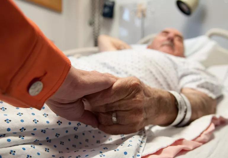 Elederly man in hospital bed with family holding hand