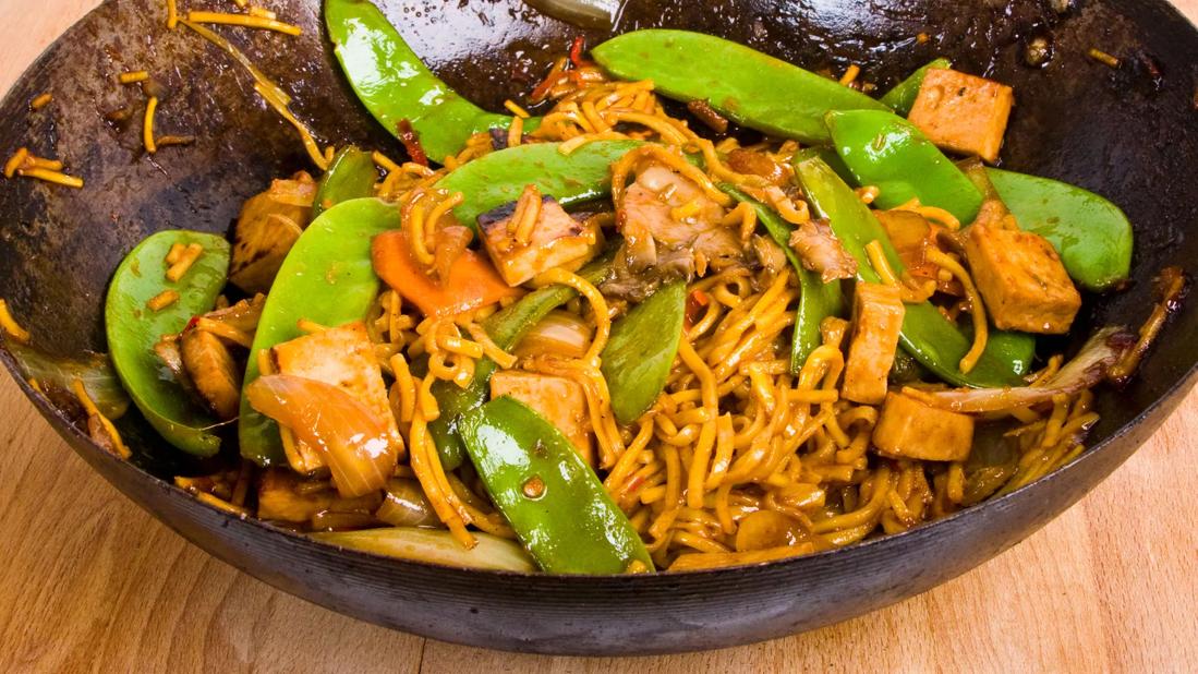 Tofu noodles, pea pods and tai peanut sauce in a wok skillet