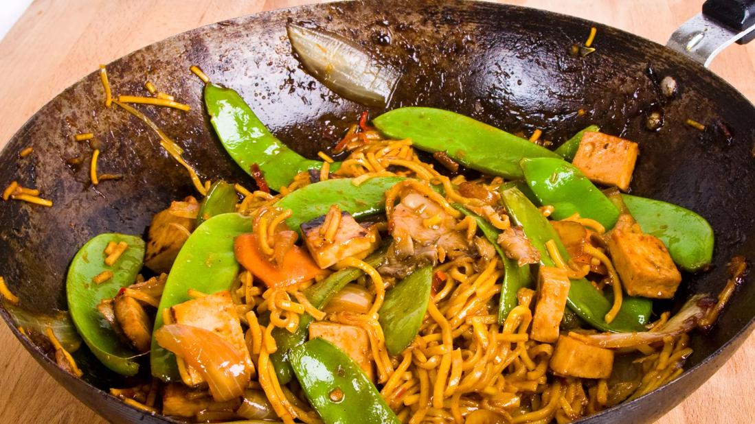 Tofu noodles, pea pods and tai peanut sauce in a wok skillet