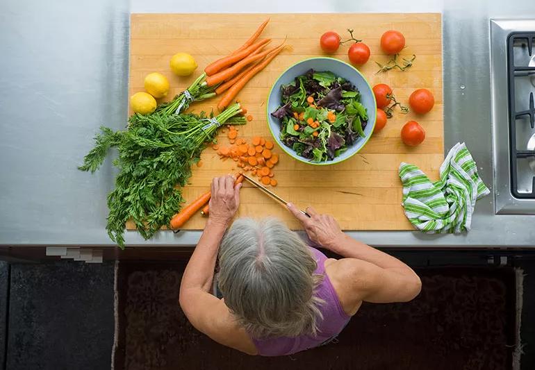 Aerial view of a person chopping carrots on a cutting board surrounded by vegetables