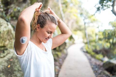 Person wearing a glucose monitor on their arm, preparing to walk outside