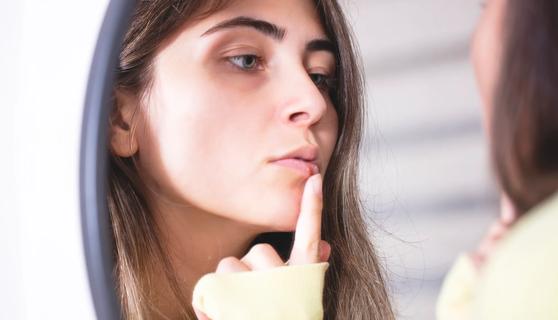 Person looking in mirror at a sore on their lip