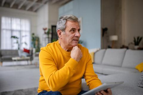 Older person sitting in living room thinking and researching on tablet