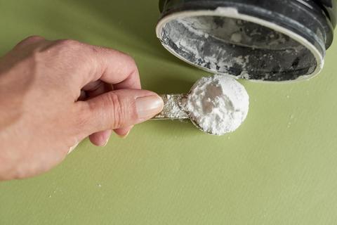 Hand with a scoop, scooping out white supplement powder from a container