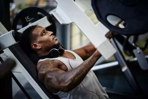 Muscular person using weight machine in gym, headphones around neck