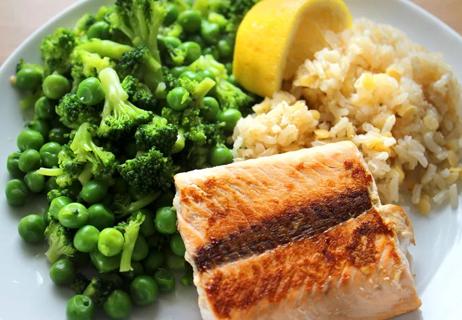 Healthy meal of salmon, brown rice and broccoli with peas on a white plate.