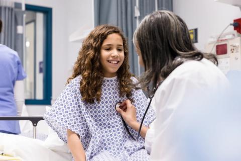 Adolescent patient sitting on hospital bed while provider uses stethoscope