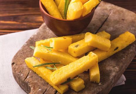 Baked polenta fries on a wooden cutting board with the rest of the fried in a bowl in the background.