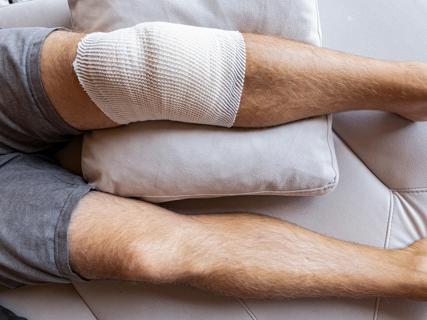 Person resting on couch with bandaged knee elevated on couch pillow