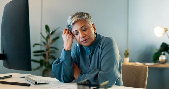 Person sitting at work desk, eyes closed, holding glassess