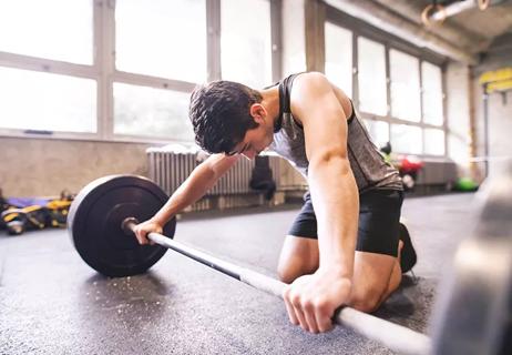 person kneeling on gym floor while hanging head and gripping a barbell