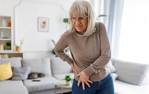 Older person standing in living room grasping hip in pain