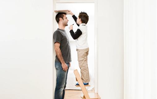 Child on stepstool measuring the height of a male adult in doorway