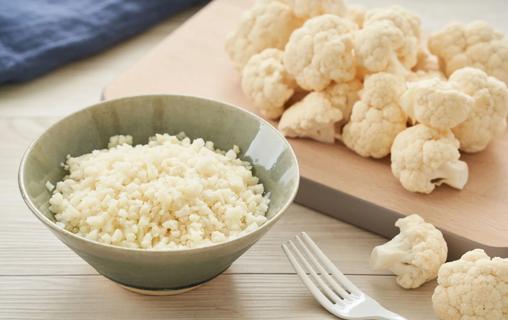 Riced cauliflower in a bowl, with cauliflower florets on cutting board