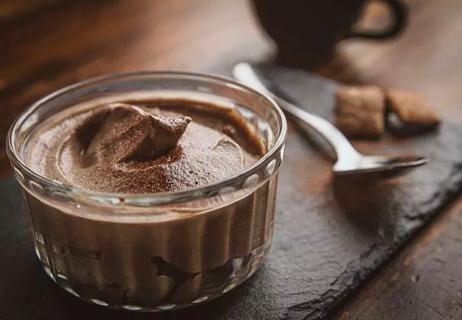 Glass bowl of chocolate mousse, with spoon on table