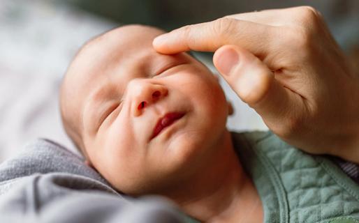 Face of sleeping newborn baby, face being lightly touched by caregiver hand