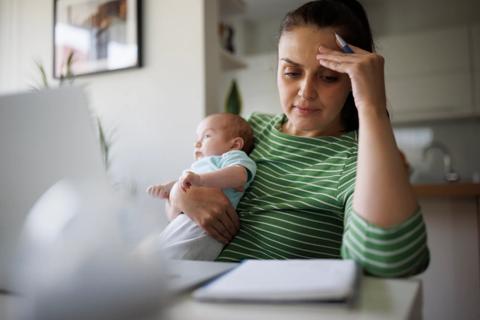 Caregiver holding newborn while also reviewing paperwork at home