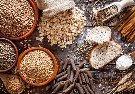 Various whole grain carbs including oats, wheat pasta and grains displayed on a wooden table.