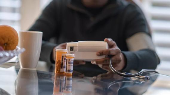 Man sitting at kitchen table with blood pressure monitor and pill bottles