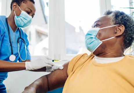 Elderly person receives vaccine in arm from health professional.