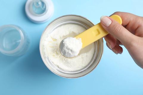 Close up of hand holding a scoop of powder baby formula over container of powder baby formula