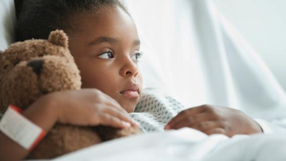 child holding teddy bear in hospital bed