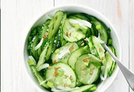 Cucumbers with sesame seeds in white bowl with fork.