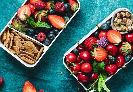 Two bento boxed filled with colorful stawberries, blueberris, cherries, nuts and wheat crackers.