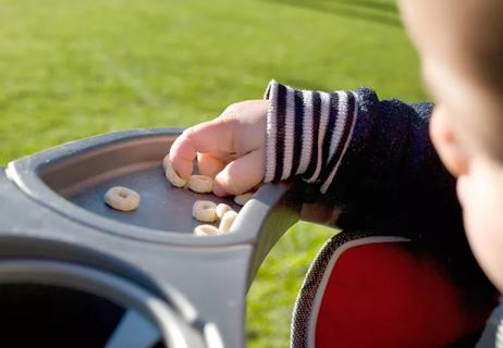 Baby pinches cereal pieces to eat while sitting in stroller.
