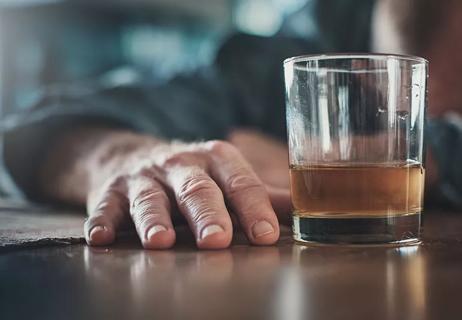 A close up of a person's hand and a half drunken glass containing an unknown, brown liquid