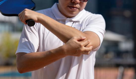 Person holding tennis paddle, grabing elbow in pain