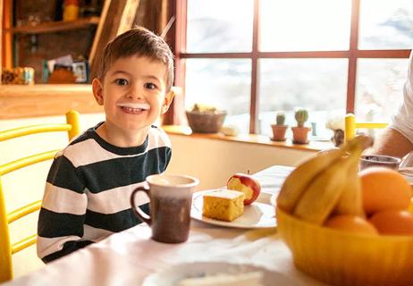 A child with a milk mustache grinning while having a snack of an apple and cornbread