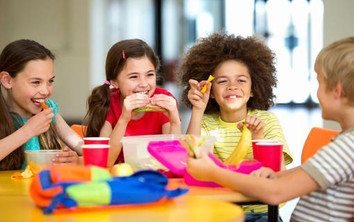 Happy elementary school kids smiling, eating lunches at table