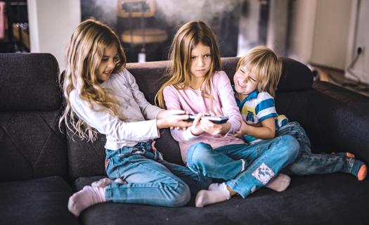 Three siblings sitting on couch fighting over TV remote control