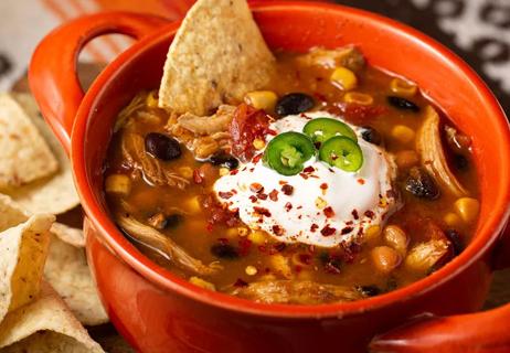 Top view of a bowl of chili topped with sour cream and jalapeños with tortilla chips for dipping.